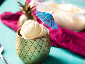 Several scoops of fresh pineapple ice cream, served in a brass-finished chalice with a diamond-etched pattern. The ice cream is garnished with a paper umbrella.