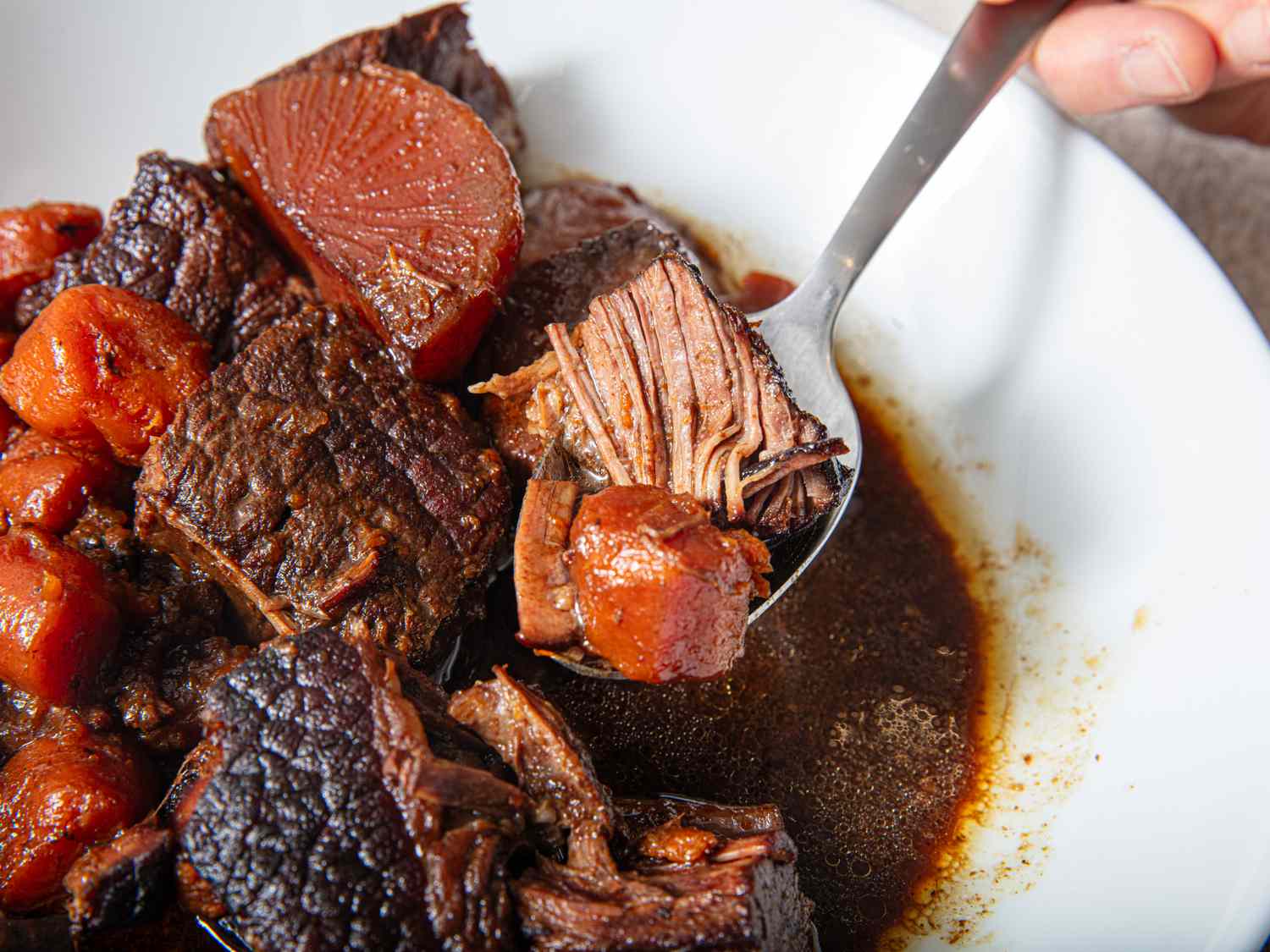 Spoon lifting beef chunks and vegetables from a bowl of stew