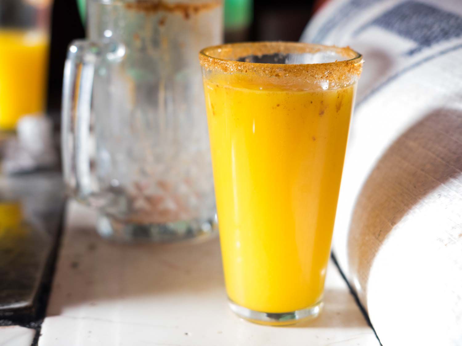A rimmed pint glass of bright-orange pulque curado.