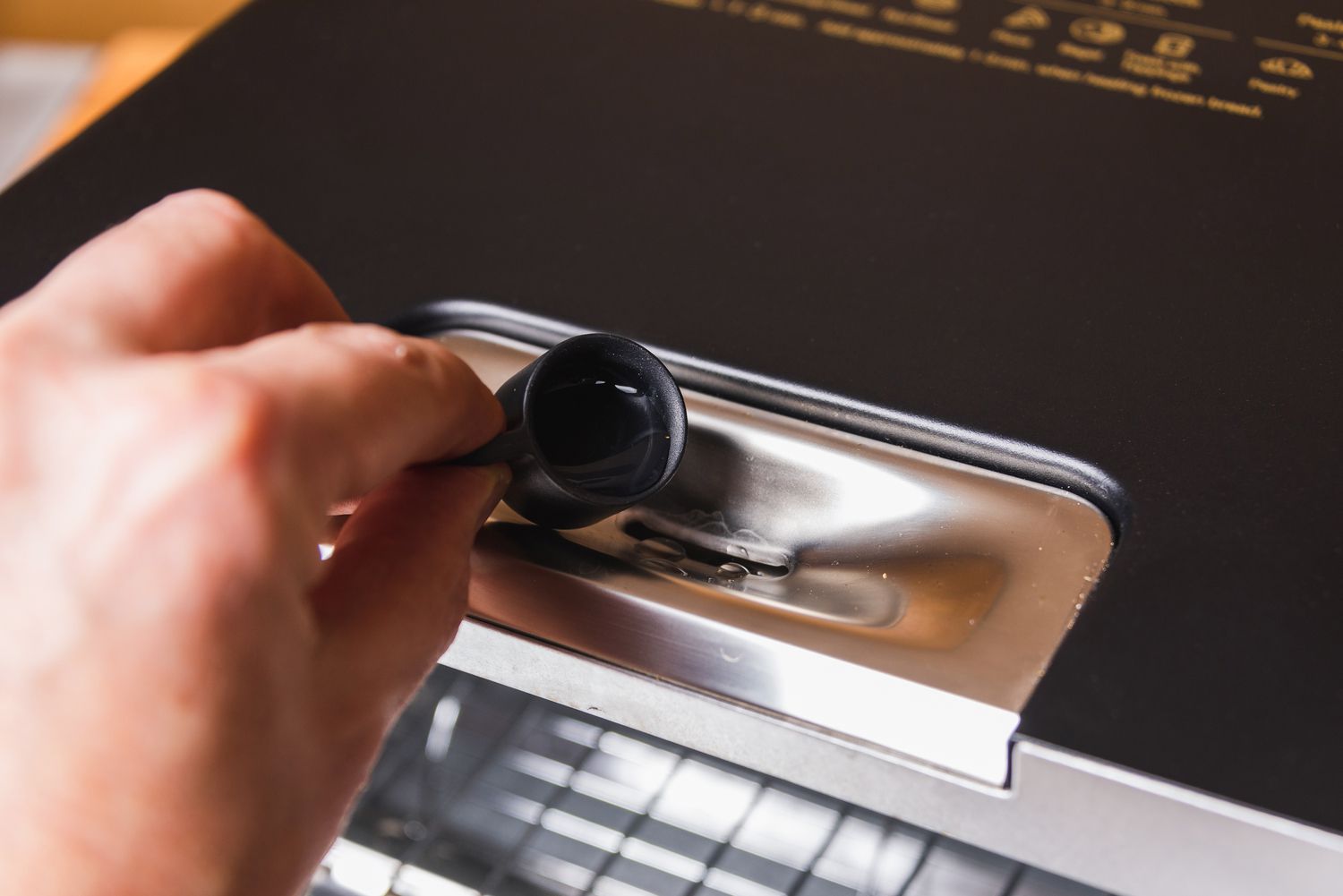 A hand using a tiny mug to add water to a slot at the top of the Balmuda Toaster