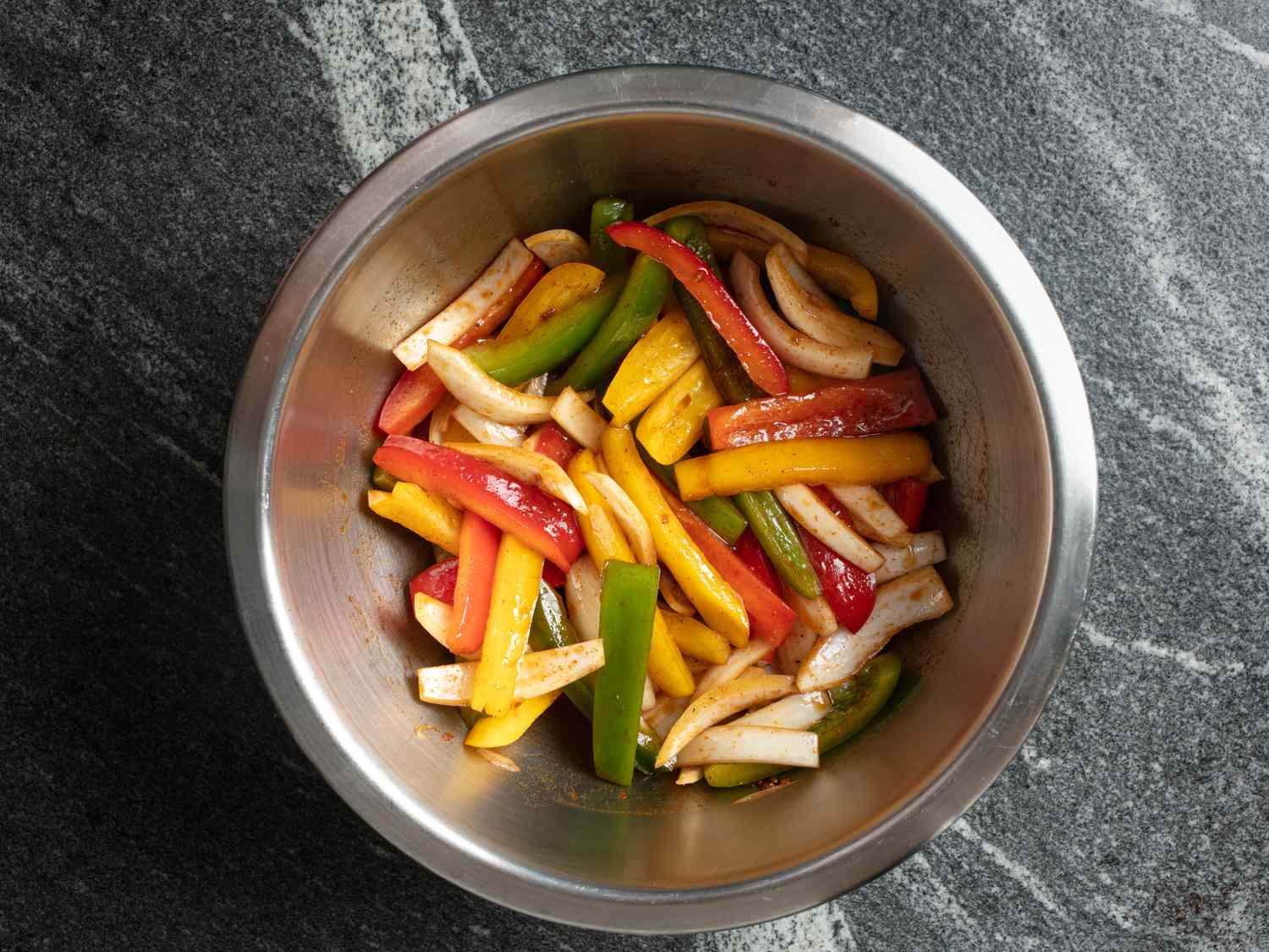 Metal bowl filled with sliced peppers, onions, and fajita marinade.