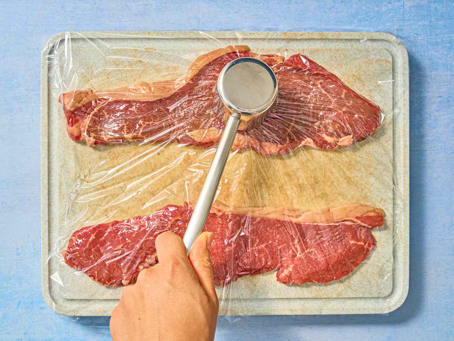steak under plastic wrap being pounded with mallet 