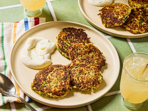 A plate of zucchini pancakes served with a dollop of yogurt, accompanied by a beverage and a colorful napkin