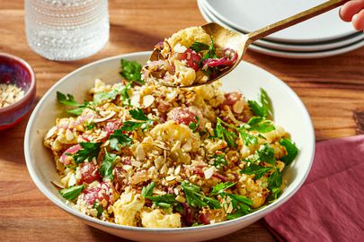A dish of roasted cauliflower with grapes herbs and nuts being scooped with a spoon