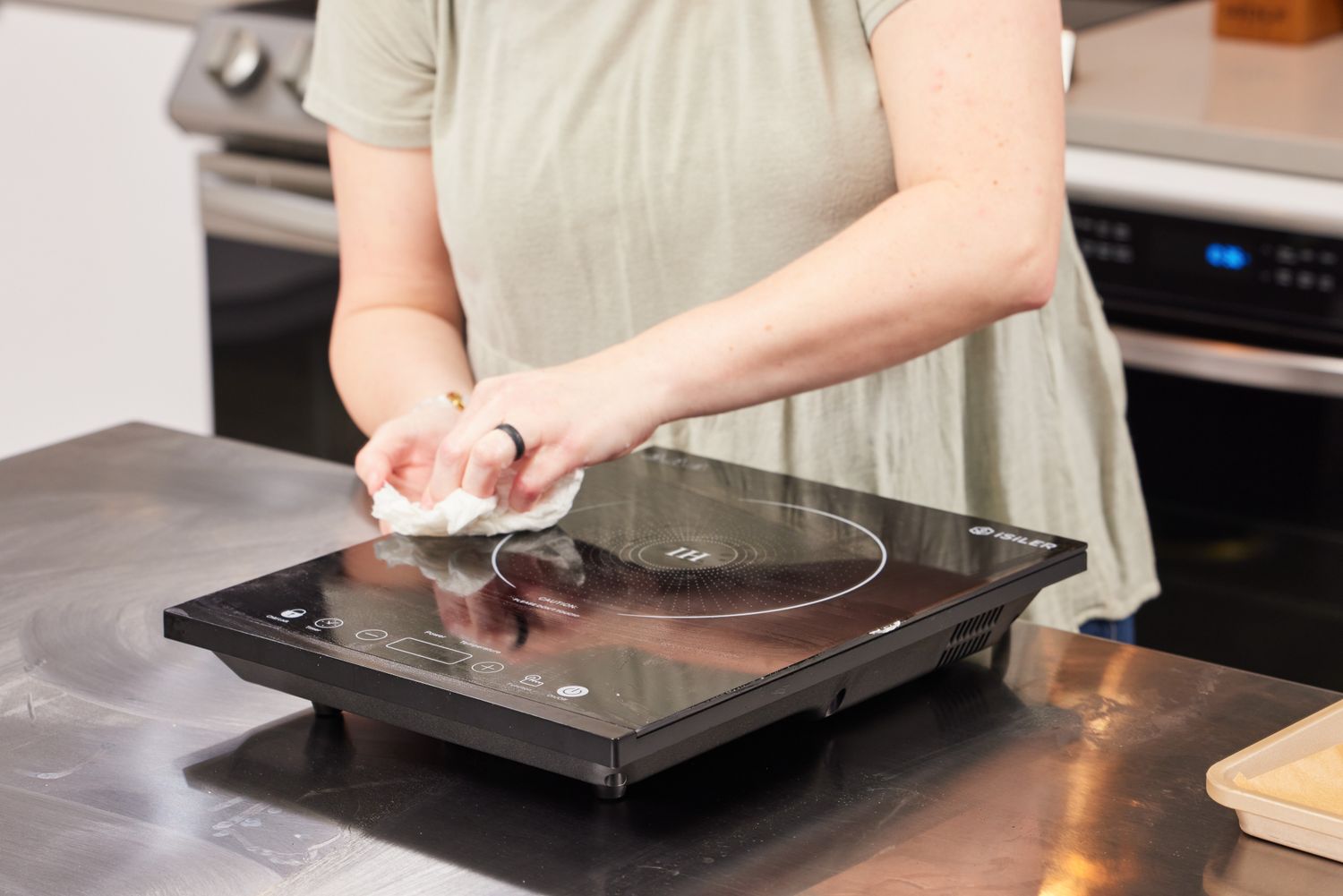 A person cleaning a portable induction cooktop with a cloth