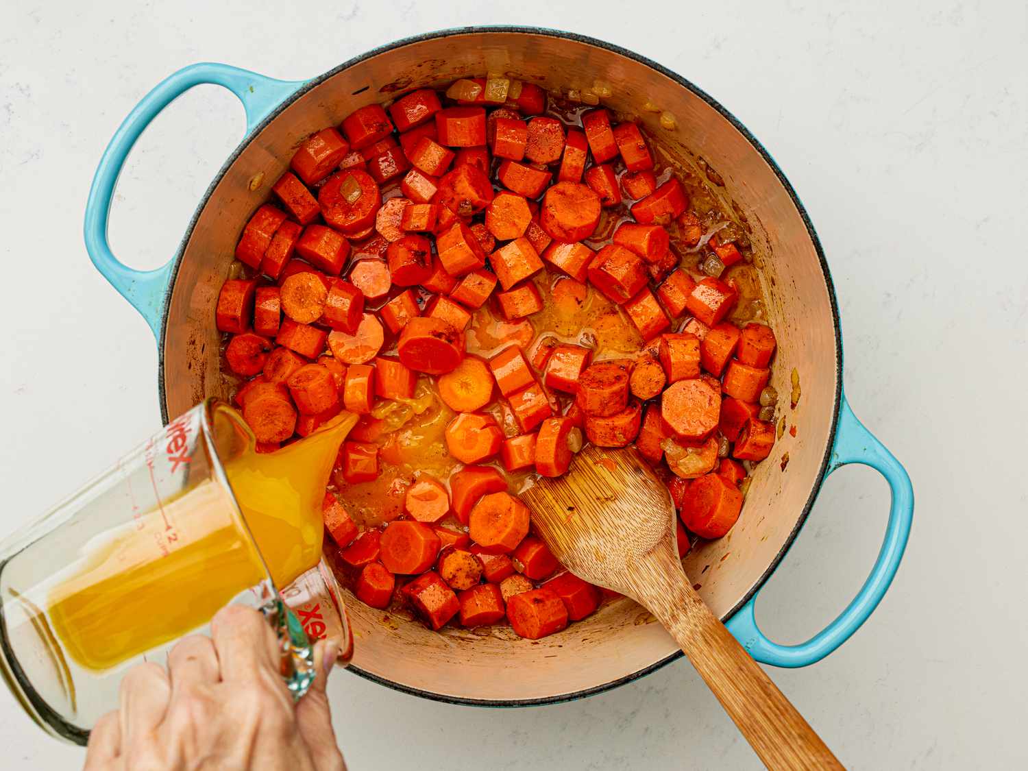 Overhead view of adding orange juice to carrots and onions