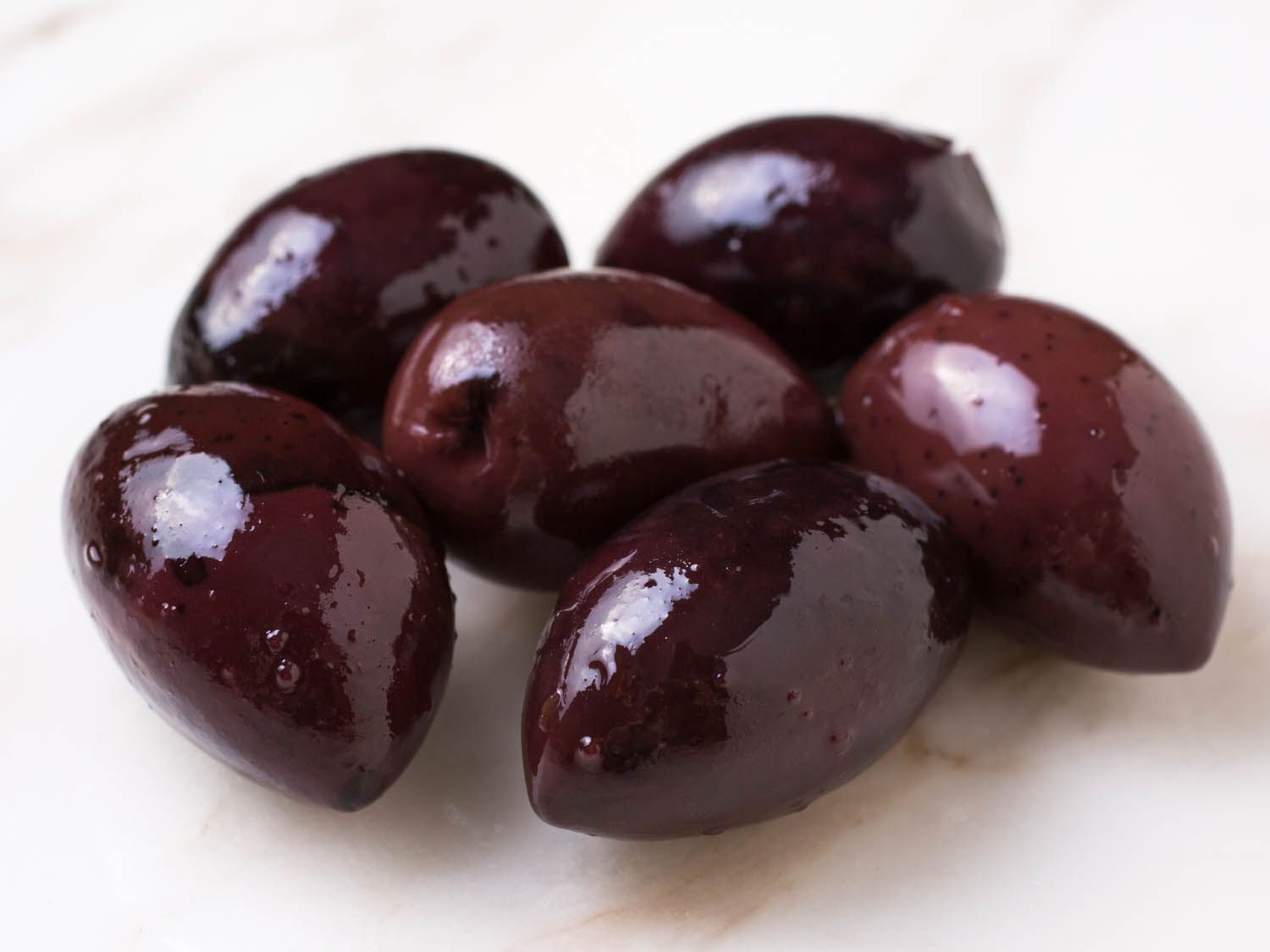 Closeup of small pile of shiny black Kalamata olives on marble