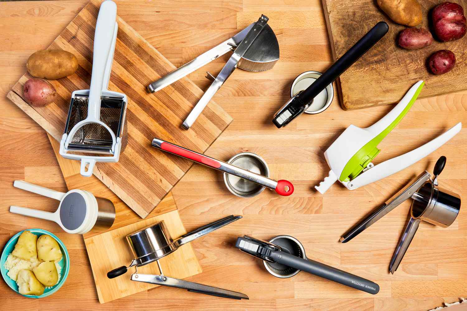 Several potato ricers and whole potatoes on a wooden countertop.