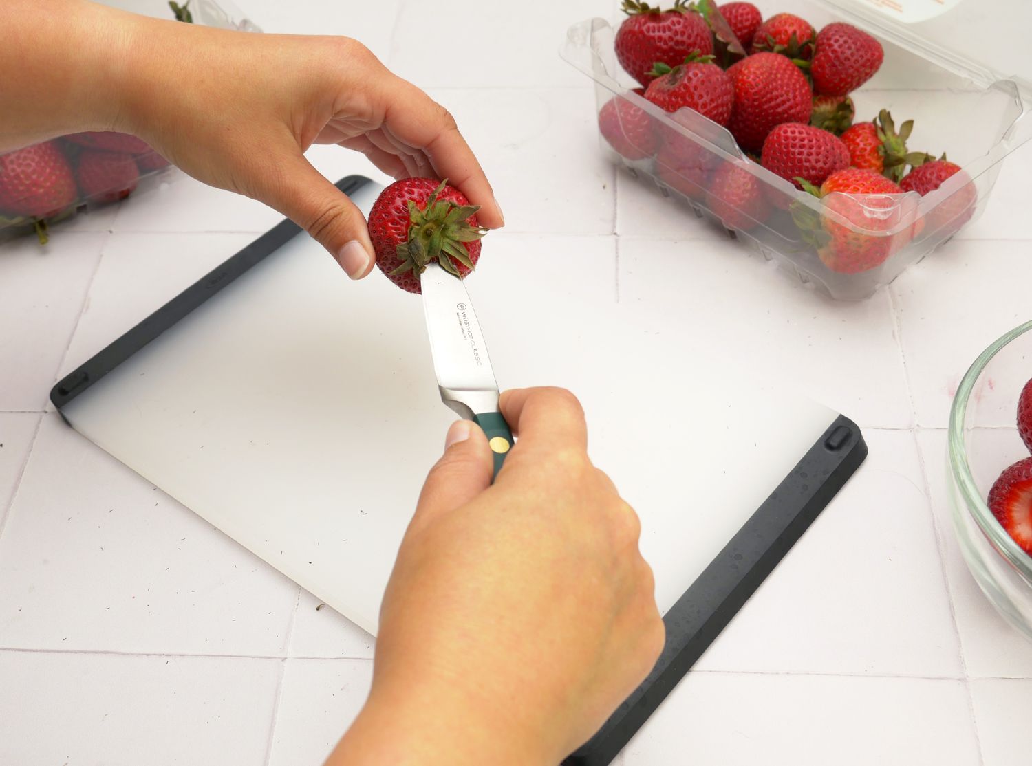 A paring knife coring a strawberry