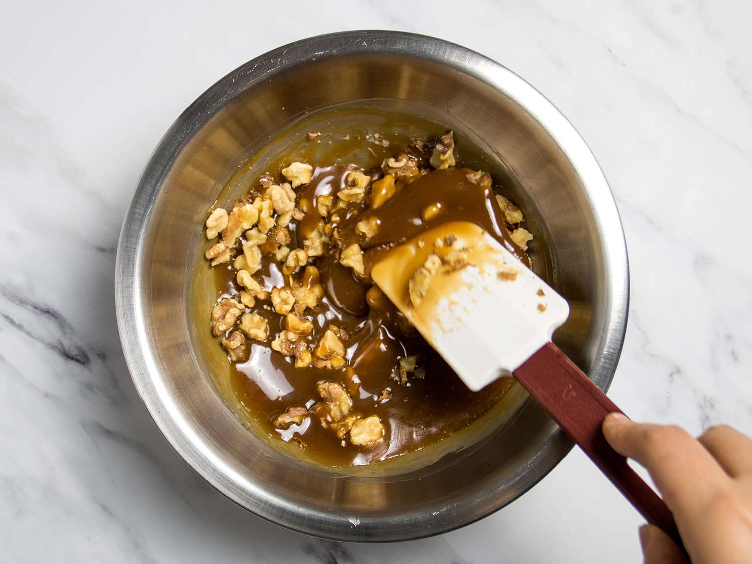 Walnuts being stirred into the finished caramel, which is thick and glossy.
