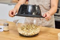 A person removes the lid on the West Bend Stir Crazy Electric Hot Oil Popcorn Popper