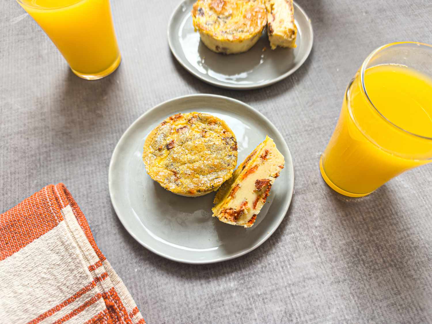 Two plates with muffin tin bacon egg bites next to glasses of orange juice