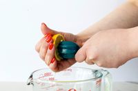 A person juices a lemon over a glass Pyrex cup using a blue ZAK! Handheld Citrus Reamer.