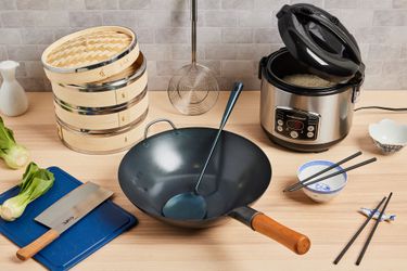 a wooden countertop with a rice cooker, wok chuan, wok, cleaver, and more. 