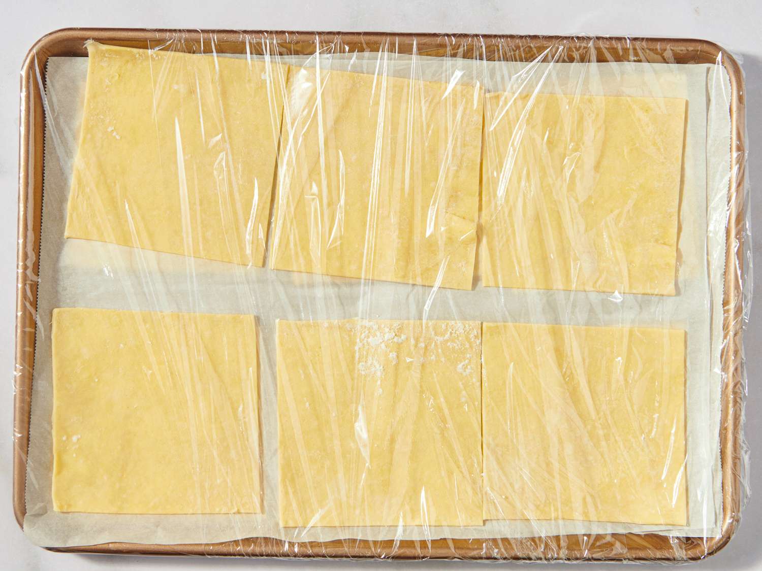 Unbaked pastry rectangles on a baking sheet covered with plastic wrap