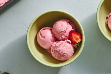 Three scoops of strawberry ice cream in a ceramic bowl, with half of a fresh strawberry.