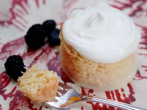 Closeup of a round portion of tres leches cake. A bite of cake is suspended nearby on the tines of a fork.