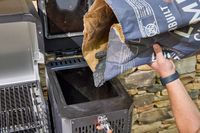 A person pours charcoal into the Masterbuilt Gravity Series 1150 Digital Charcoal Grill and Smoker