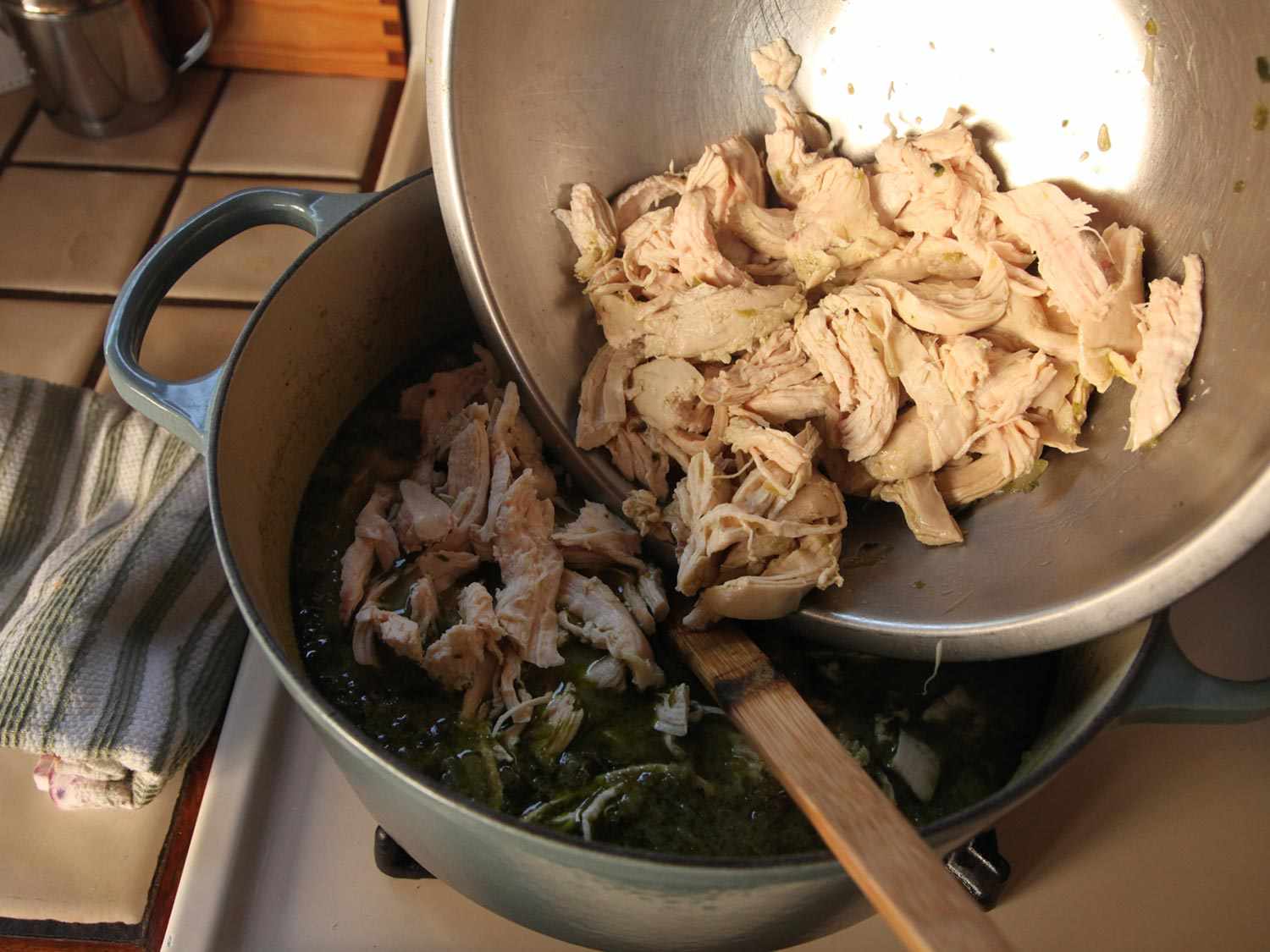Adding shredded chicken back into pot of green chili.