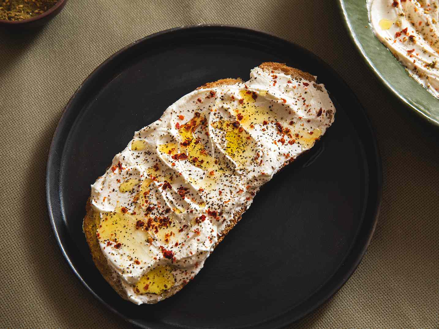 Labneh on a piece of sourdough on a plate, topped with olive oil, salt, and spices.