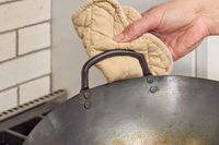 A person holds the Mammafong Pre-Seasoned Blue Carbon Steel Flat-Bottom Pow Wok by the side handle