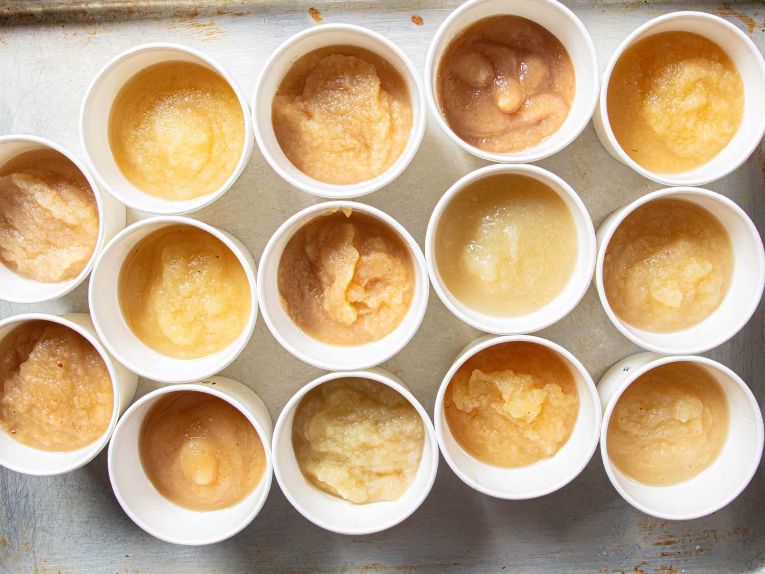 Various cups of applesauce arranged on a tray showcasing different textures and shades