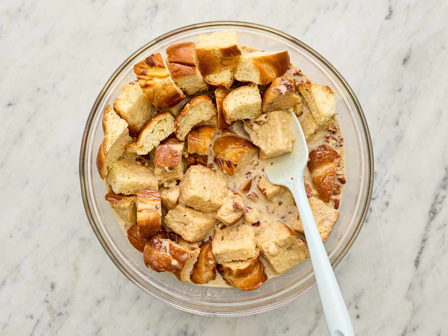 Cubed bread soaking in a milk mixture in a glass bowl with a spoon