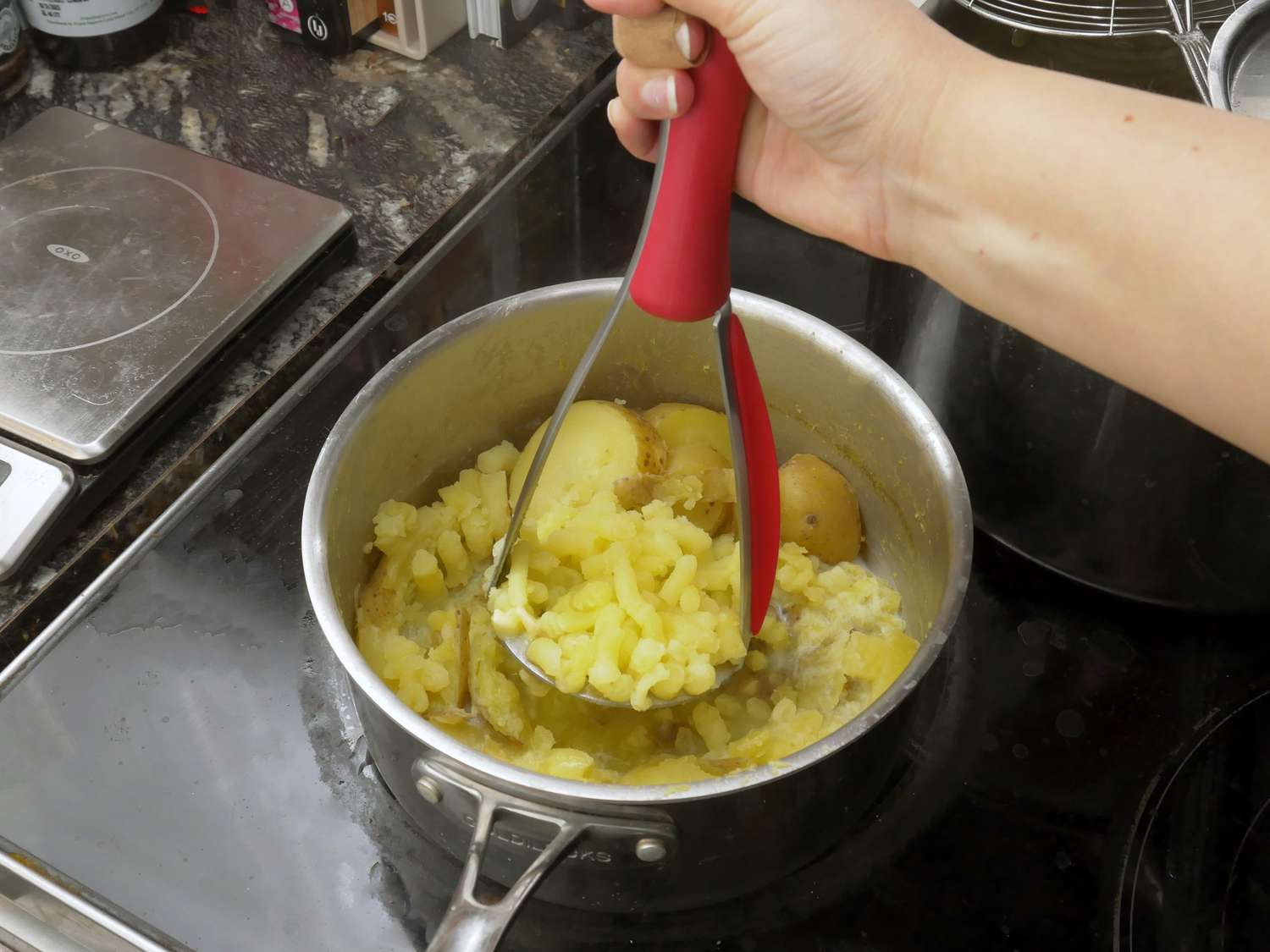 a person using the zyliss masher to mash waxy golden potatoes