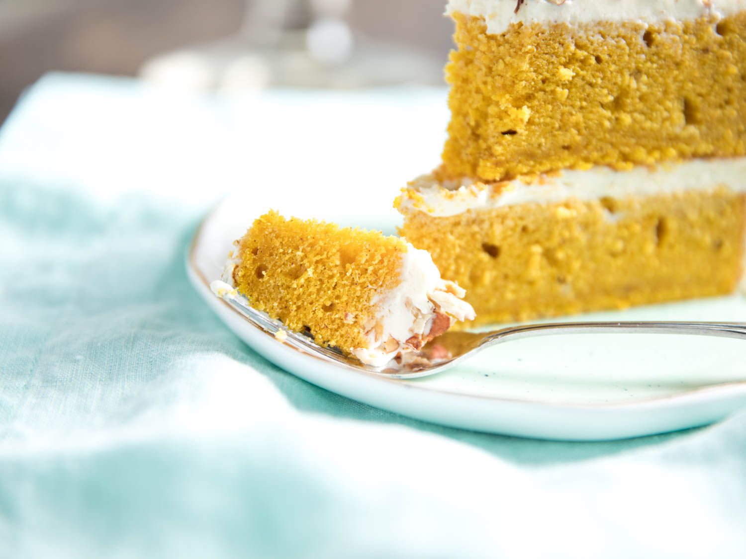 A fork spearing a bite of pumpkin layer cake, next to a wedge of cake on a plate.