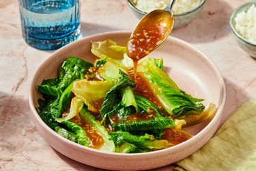 Sauteed lettuce with oyster sauce served in a bowl garnished with sauce from a spoon