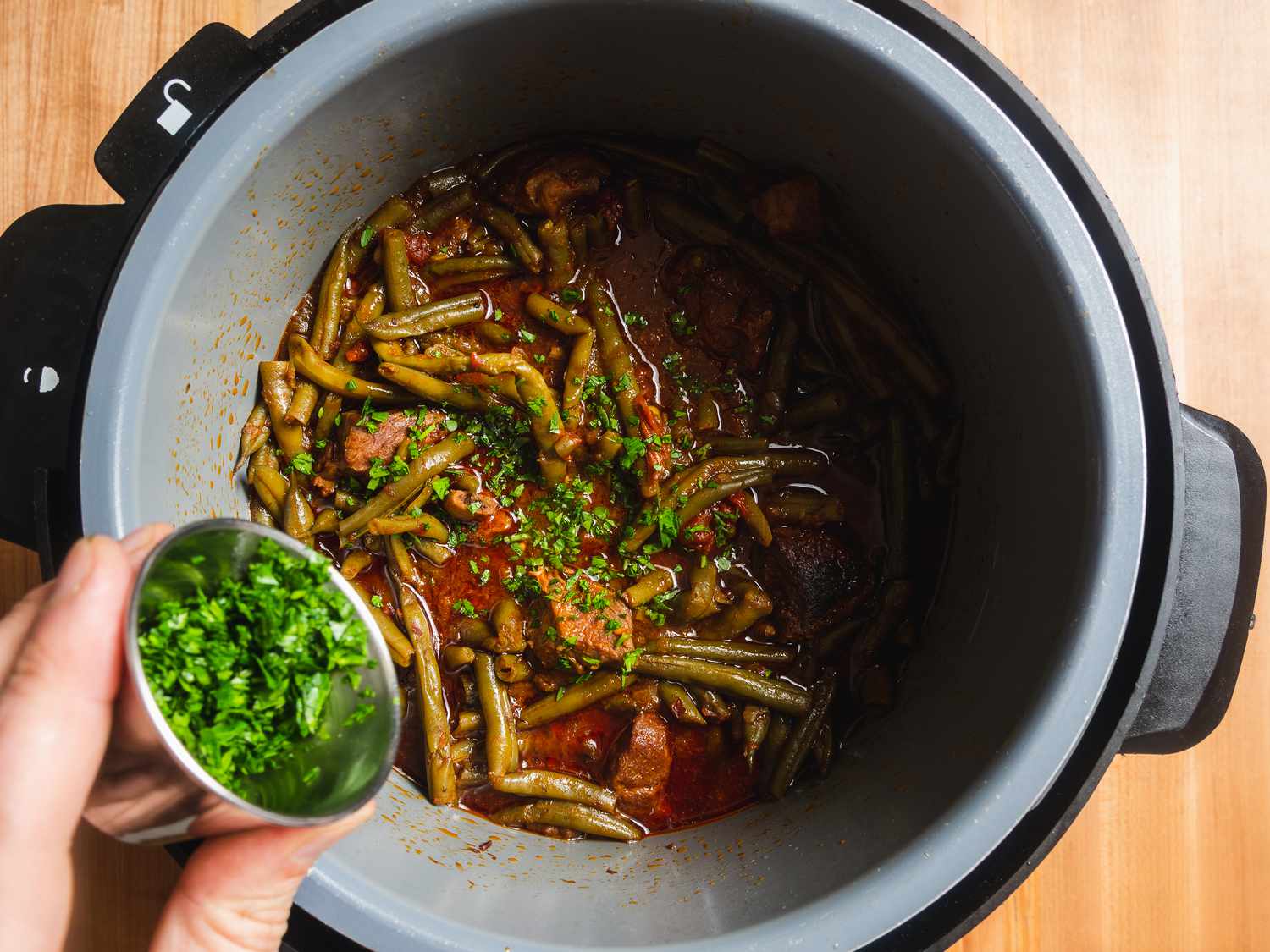 Parsley being added to finished ganach lupia in pressure cooker 