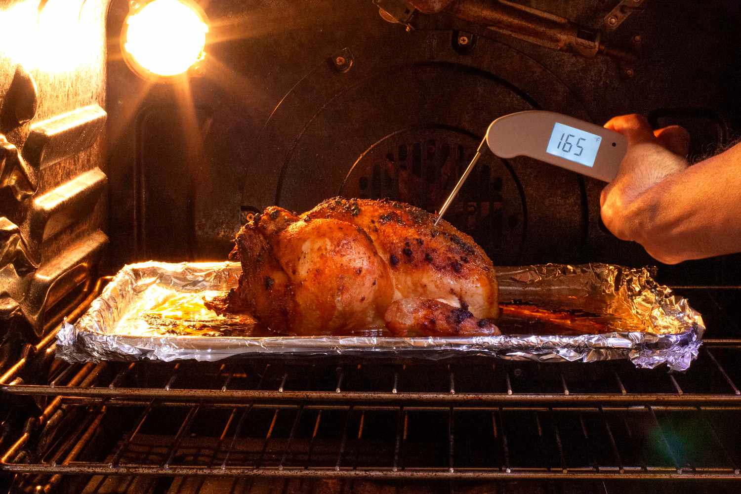A person using a white Thermapen ONE thermometer to take the temperature of chicken roasting in the oven.