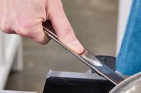 A person with their thumb on the handle of the All-Clad D3 Stainless-Steel 12-Inch Fry Pan
