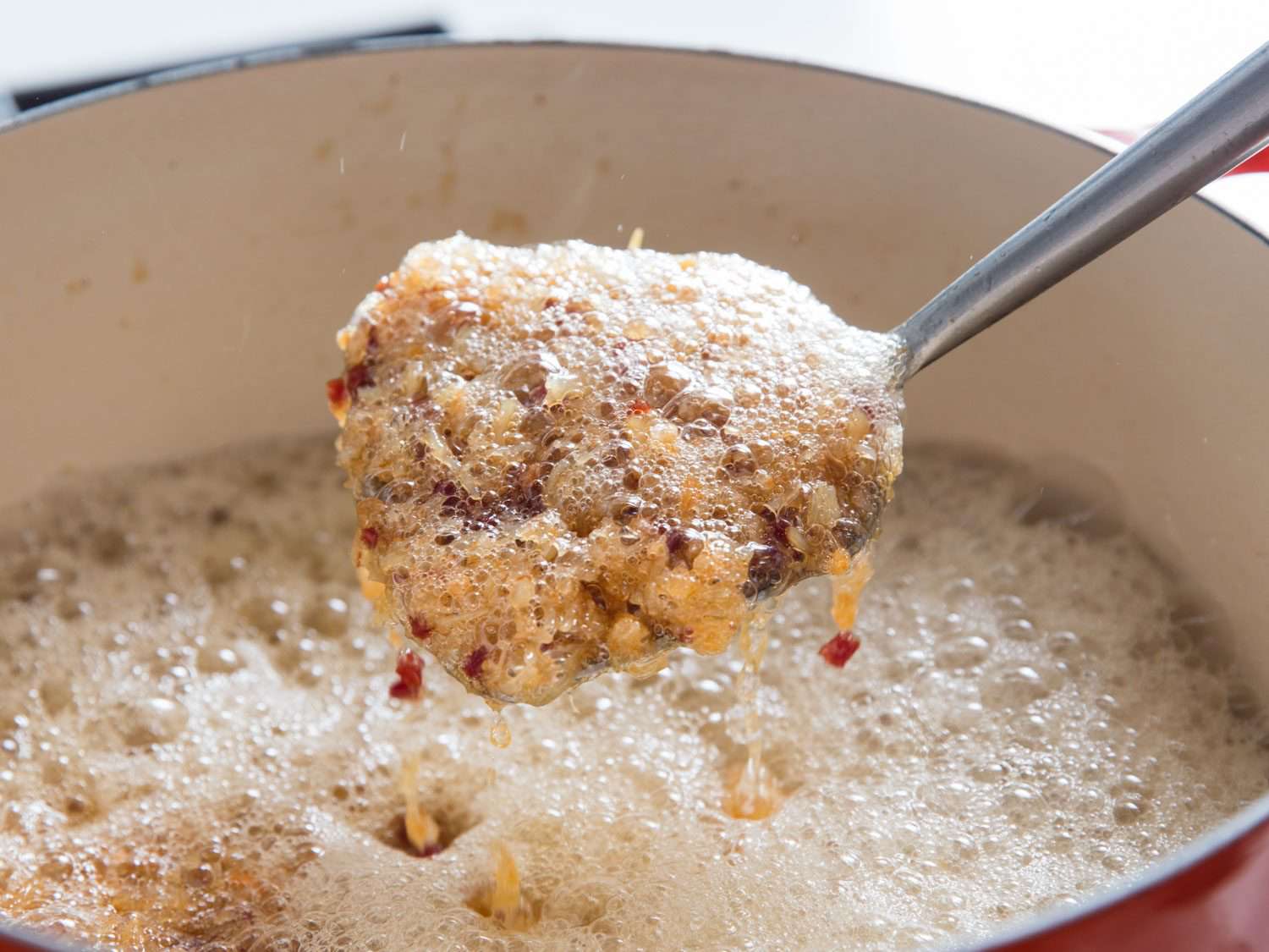 Lifting a spatula full of crispy seafood and ham out of a bubbling pot of oil.