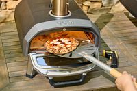 A person removes a pizza from the Ooni Karu 2 Multi-Fuel Pizza Oven