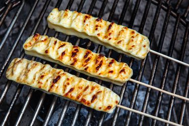 Grilled Brazilian cheese skewers on a grill grate, getting nicely browned.