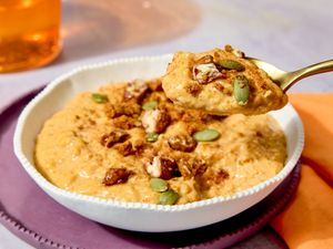 A bowl of pumpkin rice pudding garnished with nuts and seeds with a spoonful being lifted