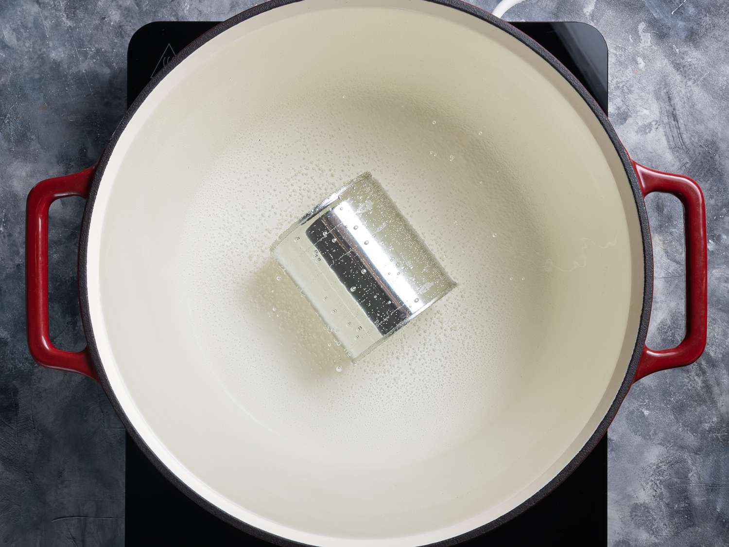 Can of condensed milk in a red cast iron pan filled with simmering water