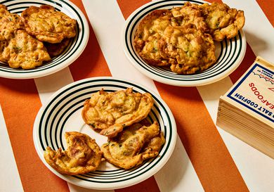 3 plates of bacalaitos and a wooden box of cod fish on red and white striped tablecloth 