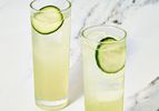 Two glasses with cucumber garnished beverages on a marble surface