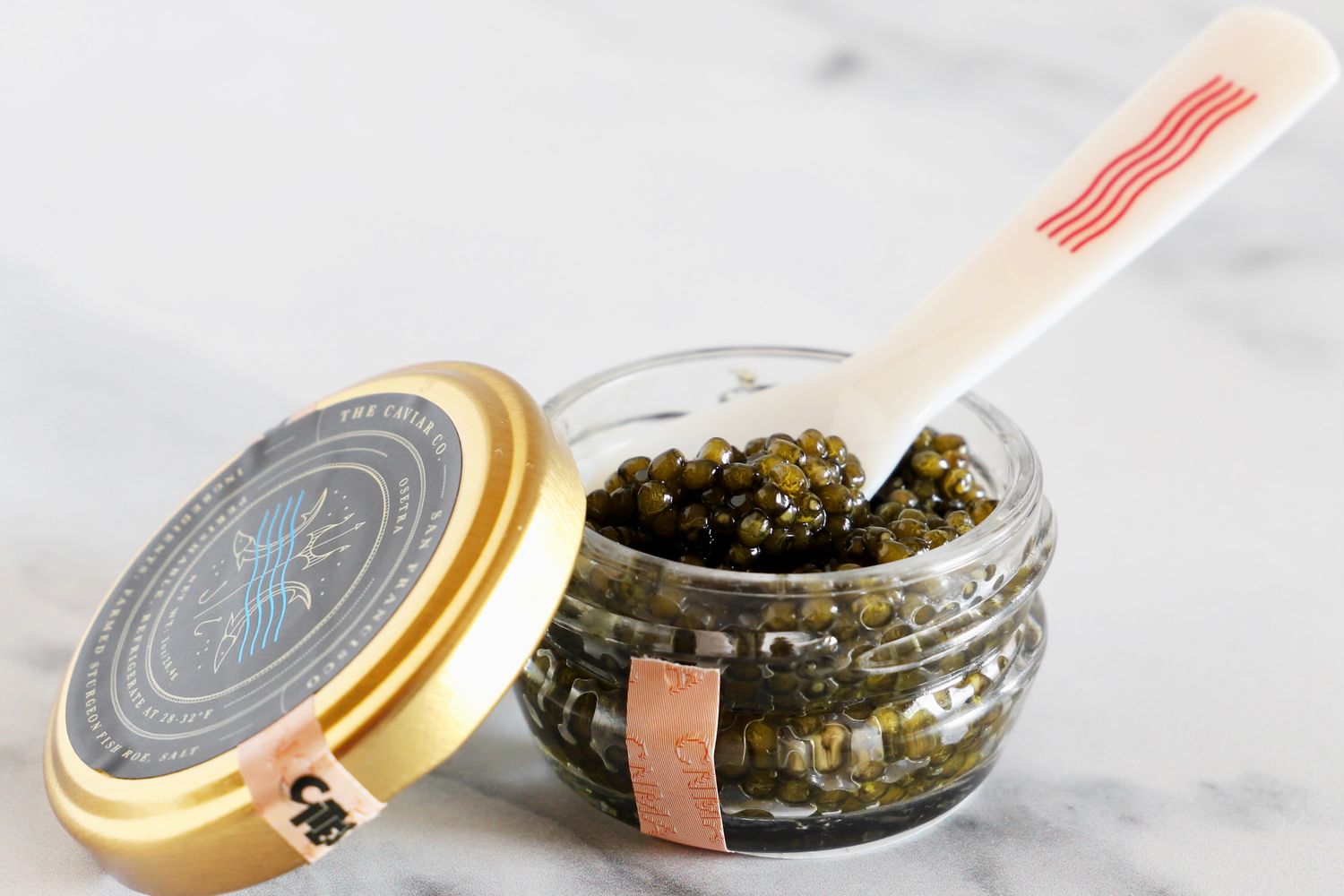 An open jar of Caviar Co osetra caviar with a mother-of-pearl spoon inside