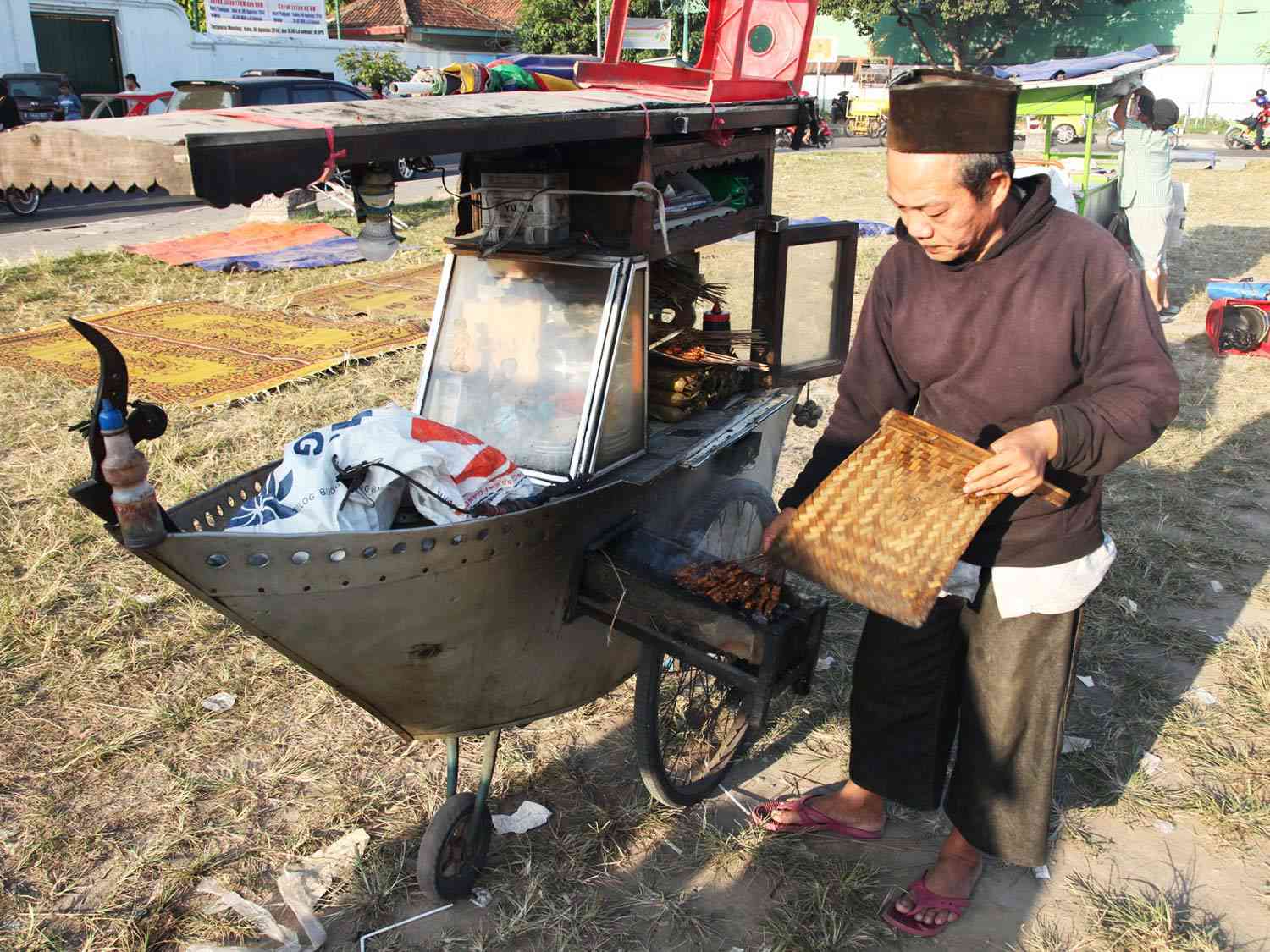 A vendor of beef satay next to a boat-shaped cart with a grill built in, in Jogjakarta, Indonesia