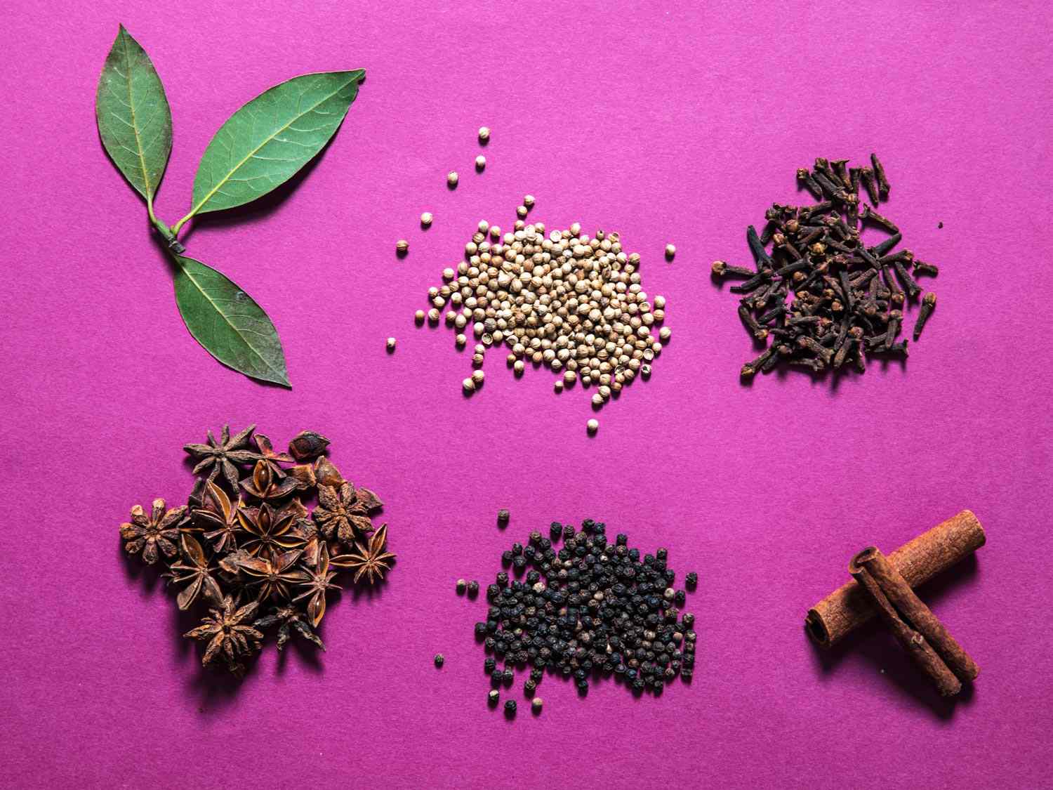 Overhead view of six spices: bay leaves, coriander, cloves, star anise, black peppercorns, cinnamon.