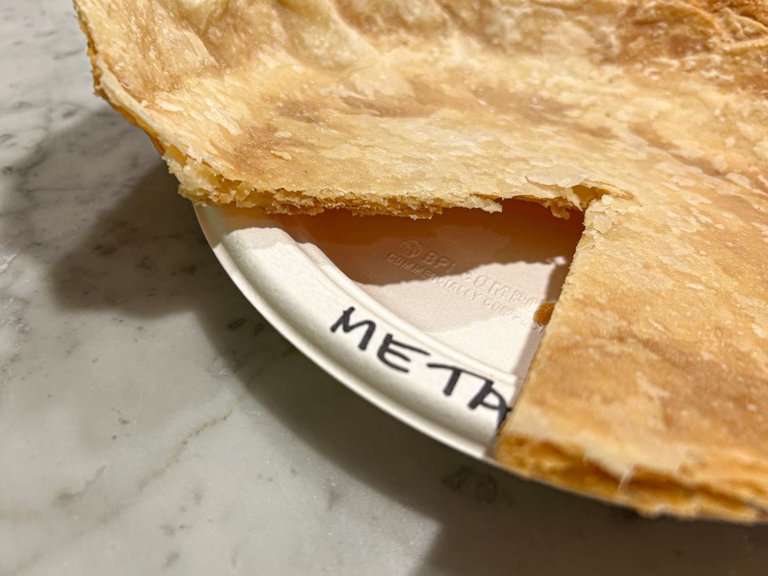 A piece of pie crust on a plate labeled META on a marble surface