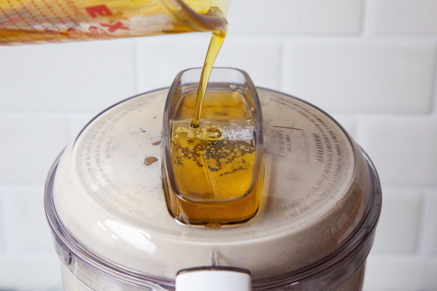 Oil being drizzled into the top of a mini food processor.