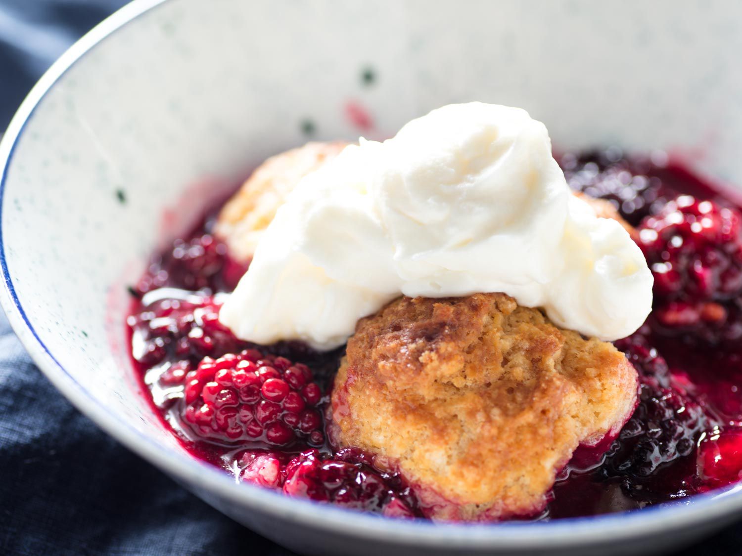 Close-up of a bowl of blackberry cobbler topped with whipped cream.