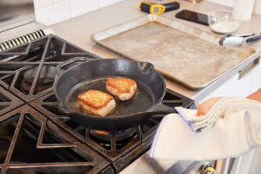 A person searing meat in a cast iron skillet on the stovetop