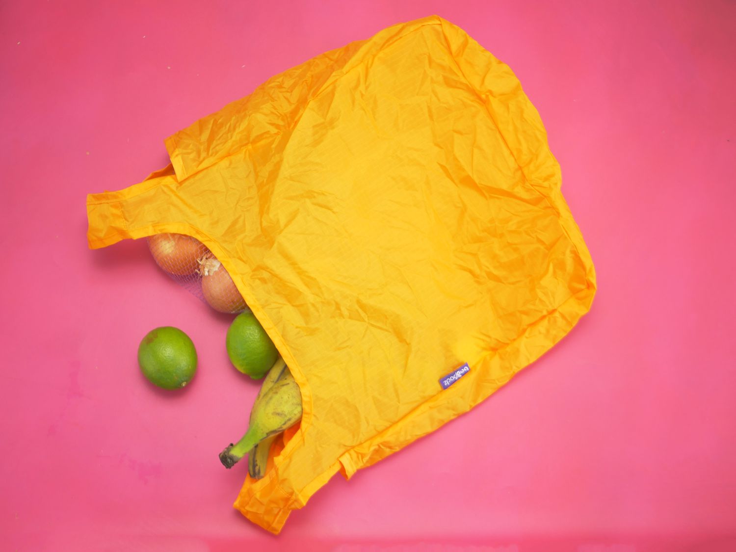 BagPodz grocery bag on its side with plantains, onions, and limes spilling out