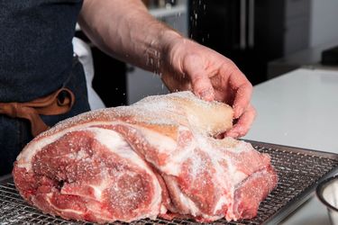 Seasoning a pork shoulder with kosher salt.