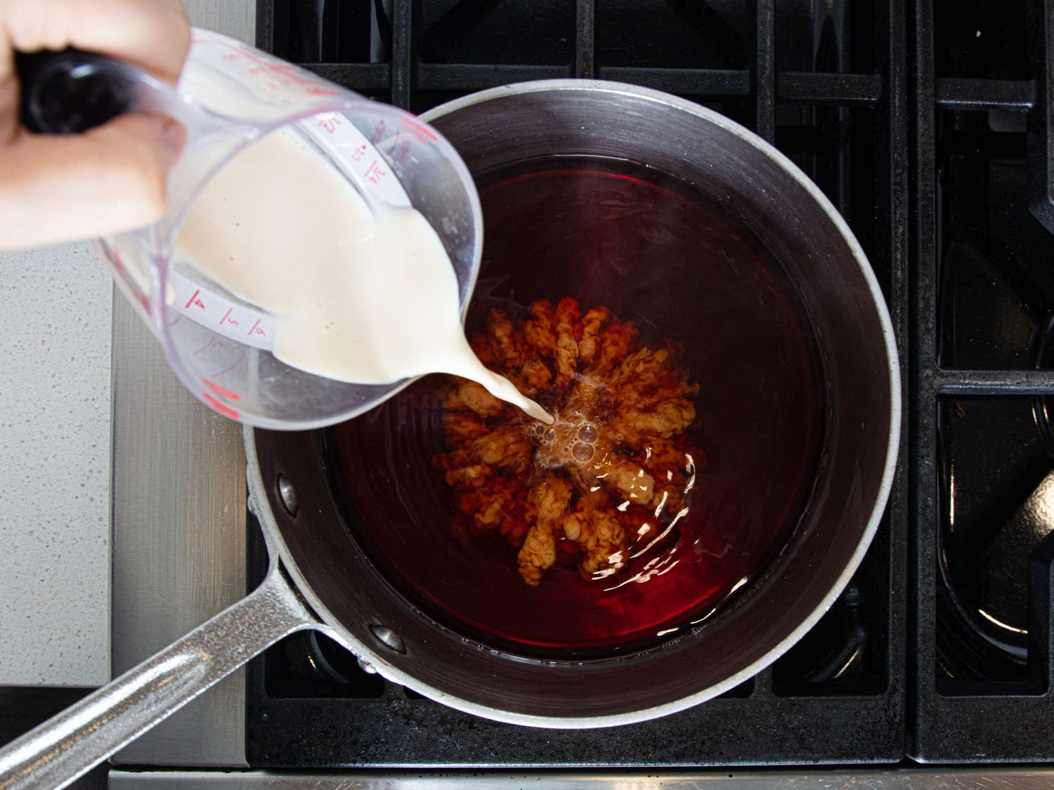 Pouring milk into a saucepan filled with heated liquid and spices on a stovetop
